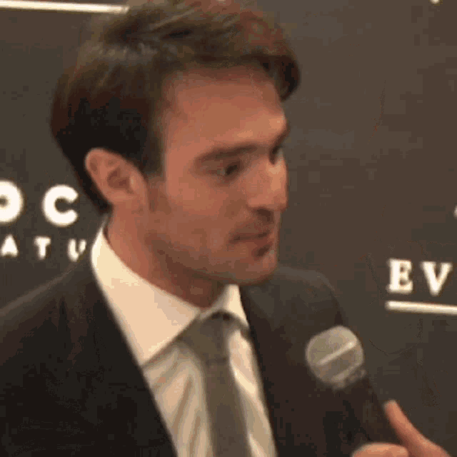 a man in a suit and tie is holding a microphone in front of a wall with the word focus on it