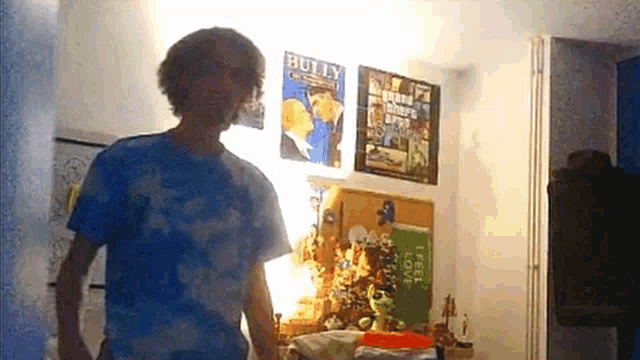 a man in a blue shirt is standing in a room with posters on the wall one of which says bully