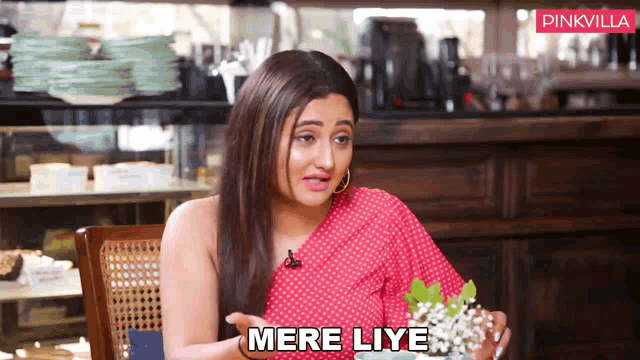 a woman sitting at a table with a sign that says mere liye in front of her