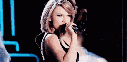 a woman is singing into a microphone on a stage in a dark room .
