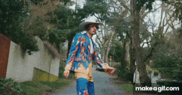 a man wearing a colorful suit and cowboy hat is walking down a street .