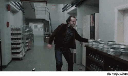a man in a red jacket is dancing in a hallway next to a shelf of film reels .