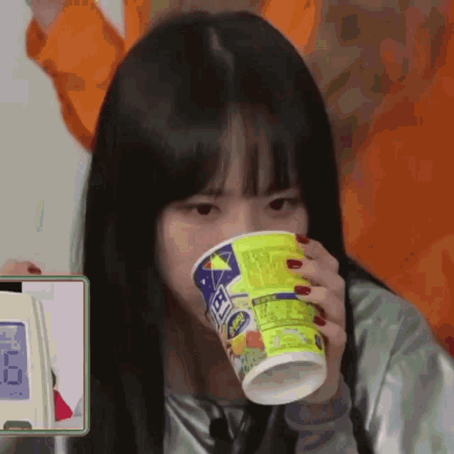 a girl with red nails is drinking from a cup with a sticker on it