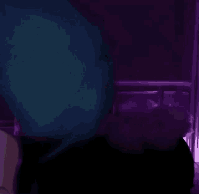 a person is sitting in a dark room with a purple light behind them .
