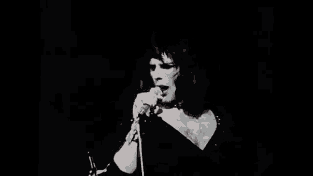 a woman is singing into a microphone on a stage in a dark room .