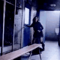 a woman in a black dress is standing in a locker room next to a bench