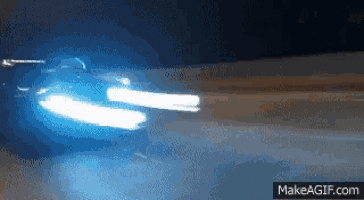 a car is driving down a road at night with a blue light coming out of its headlights