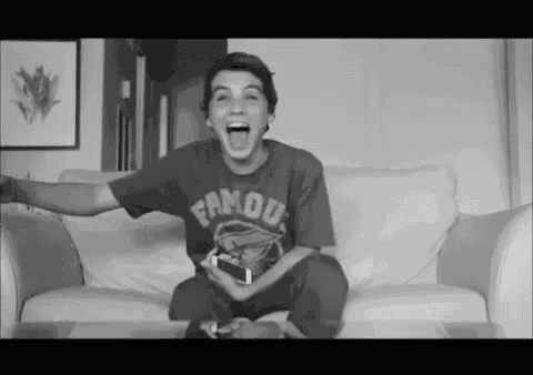 a boy wearing a famous shirt is sitting on a couch with his mouth open .