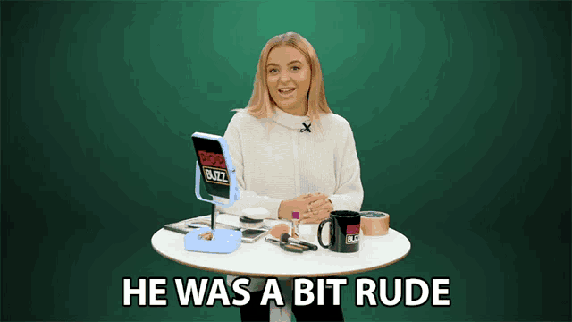 a woman sitting at a table with a mirror and a mug that says ' he was a bit rude '