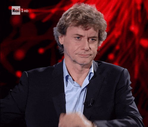 a man wearing a suit and a blue shirt is sitting in front of a red background that says rai 1 hd