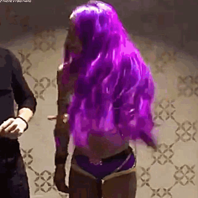 a woman with long purple hair is standing in front of a wall .