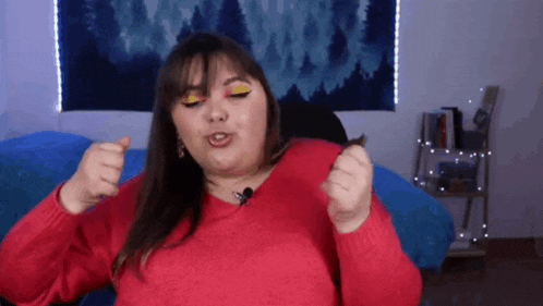 a woman in a red sweater is sitting on a bed with a microphone in her hand .