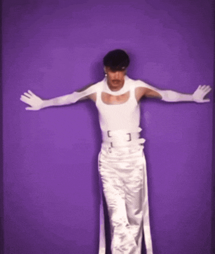 a man in a white tank top and white pants is standing in front of a purple background holding a knife .