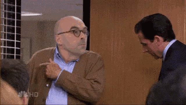 a man in a brown jacket is pointing at another man in a suit with nbc hd written on the bottom right