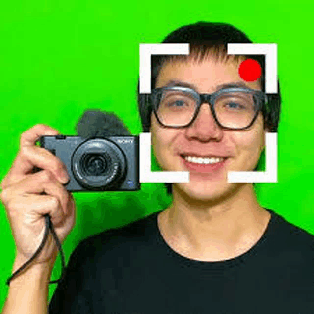 a man in glasses is holding a camera in front of his face .