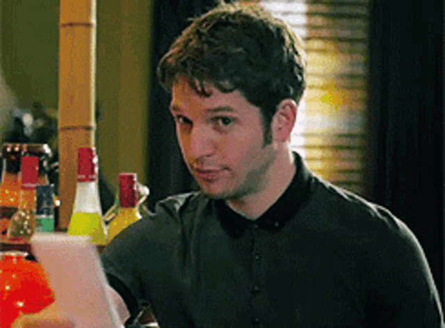 a man sitting at a table with bottles in the background looking at something
