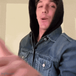 a man wearing a denim jacket and a hoodie is making a face .