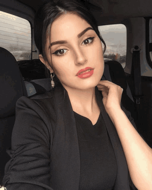 a woman wearing a black jacket and red lipstick takes a selfie in a car