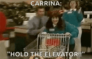 a woman is pushing a shopping cart in a store while a man holds the elevator .