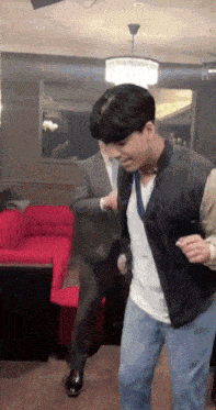 a man in a suit and vest is dancing in a room with a red couch
