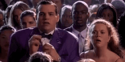 a man in a purple suit is standing in front of a crowd of people .