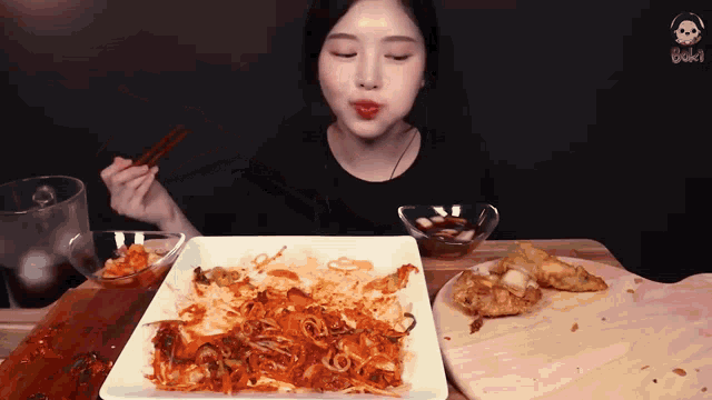 a woman eating a plate of food with chopsticks and a bowl of dipping sauce