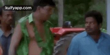 a shirtless man in a green shirt is standing next to a tractor .