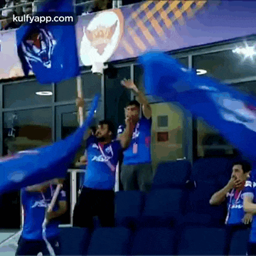 a group of men in blue shirts are holding blue flags in a stadium .