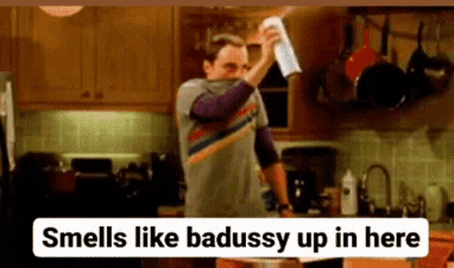 a man is holding a spray bottle in his hand in a kitchen and says `` smells like badussy up in here '' .