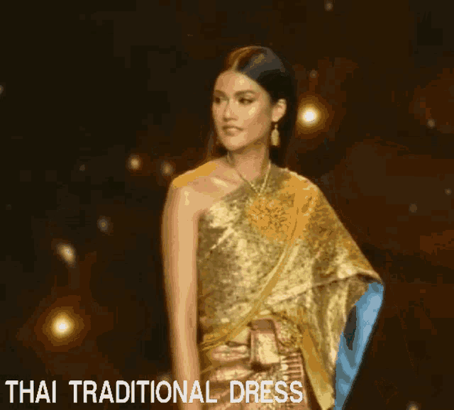 a woman in a gold dress is walking down a runway with the words thai traditional dress behind her