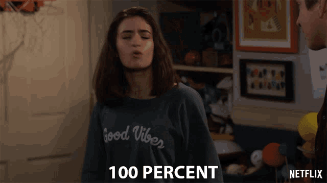 a girl wearing a sweater that says good vibes blows a kiss