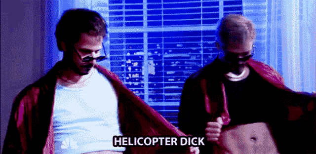 two men are standing in front of a window and one of them is holding his shirt up and says helicopter dick