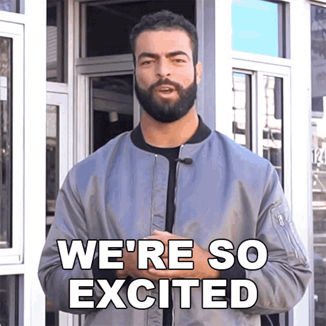a man with a beard is standing in front of a building and says we 're so excited