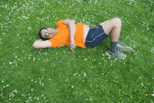 a man in an orange shirt is laying in the grass with his eyes closed