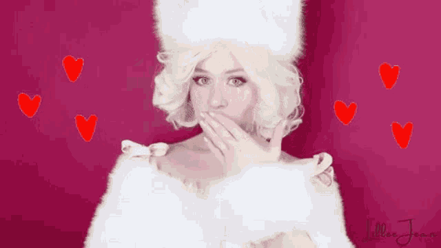 a woman in a white fur coat is covering her mouth with her hand while hearts are flying around her .