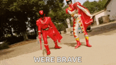 two red power rangers are standing next to each other on a sidewalk and talking .