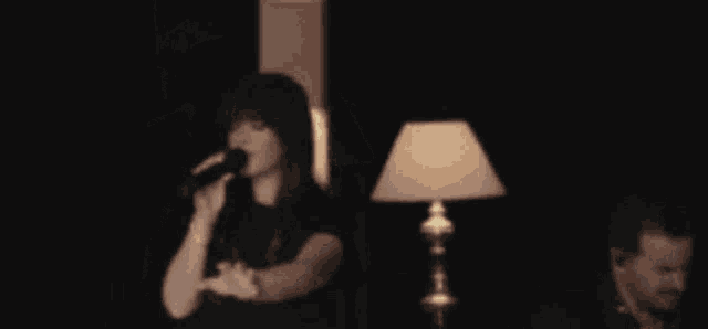 a woman is singing into a microphone while a man is playing a piano in the background .