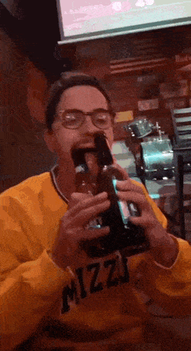 a man wearing a yellow sweatshirt that says mizzj is drinking a beer