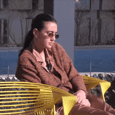 a woman wearing sunglasses sits in a yellow chair outside