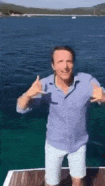 a man in a blue shirt and white shorts is standing on a dock in front of a body of water .