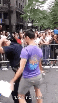 a man in a purple shirt is standing next to a police officer in front of a crowd .