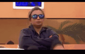 a woman wearing sunglasses is sitting with her arms crossed in a room .