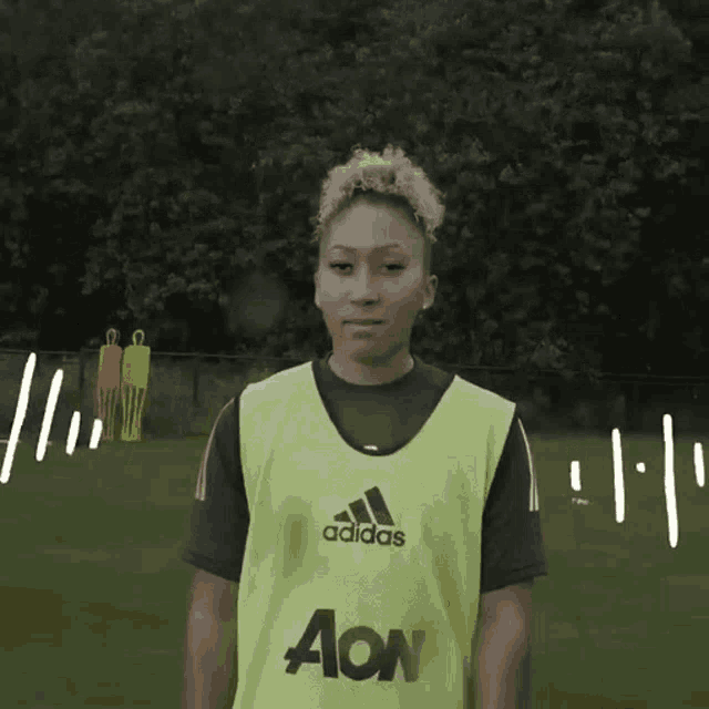 a woman wearing a yellow adidas shirt stands in front of a green field