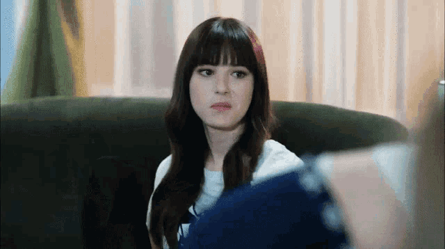 a woman with bangs is sitting on a couch and making a face .
