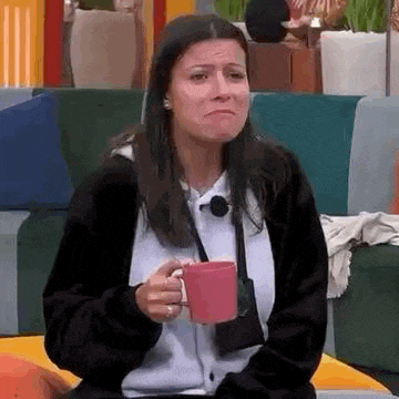 a woman is sitting on a couch holding a pink cup of coffee and crying .