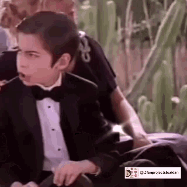 a young boy in a tuxedo and bow tie is sitting on a chair .