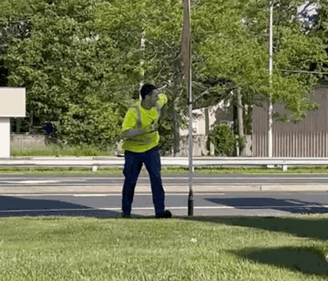 a man in a yellow vest is standing in the grass next to a street .