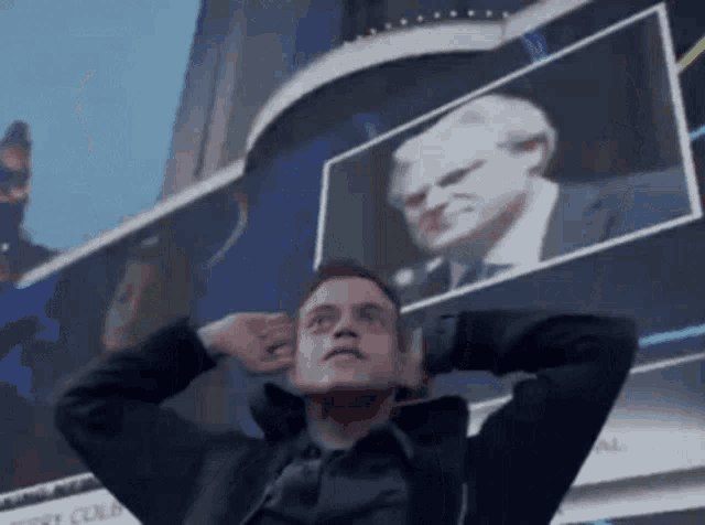 a man is covering his ears in front of a large screen with a picture of a man on it