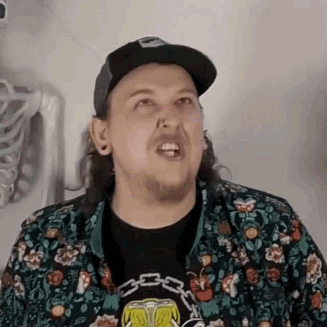 a man wearing a hat and a floral shirt is making a face .