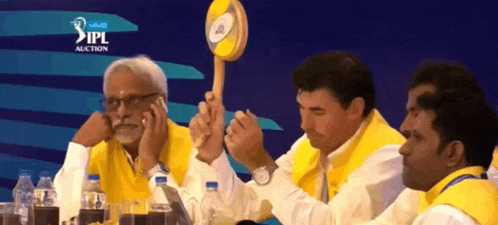 a group of men sitting at a table with a sign that says ipl auction on it